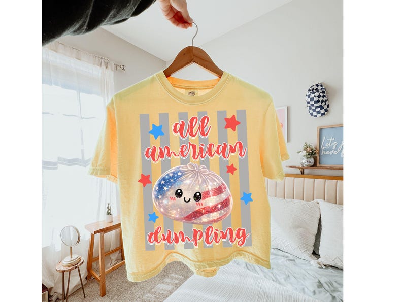May include: Yellow t-shirt with the text "all american dumpling" in red script. The graphic features a dumpling with an American flag design and a cute face, surrounded by stars and stripes.