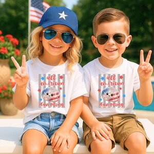 May include: Two children wearing white t-shirts with the text "all american dumpling" and a graphic of a dumpling decorated with the American flag. The girl wears a blue cap and sunglasses, and the boy wears sunglasses. They are smiling and making peace signs.
