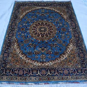 May include: A rectangular blue rug with an intricate floral pattern. The rug features a central medallion in shades of brown and cream, surrounded by a border of dark blue and cream floral designs. The rug has a fringe on the bottom edge.