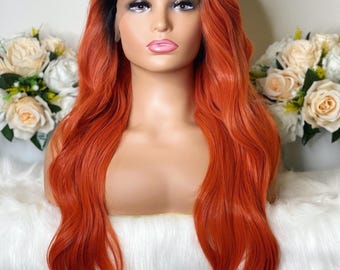 May include: A long, wavy synthetic wig featuring a vibrant orange color with dark roots. The wig is styled with a center part and a lace front construction, displayed on a mannequin head with soft facial features and light pink lips.