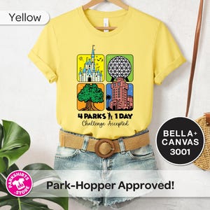 Puede incluir: Camiseta amarilla con un gr&aacute;fico que presenta cuatro iconos de parques tem&aacute;ticos y el texto "4 Parks 1 Day Challenge Accepted". La camiseta se combina con pantalones cortos de mezclilla y un cintur&oacute;n tejido. Un bolso redondo cuelga en el fondo.