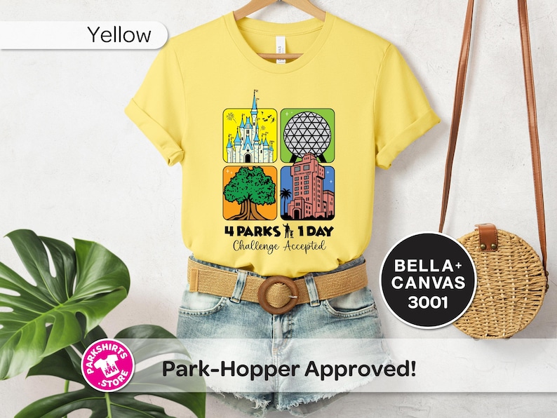 Puede incluir: Camiseta amarilla con un gr&aacute;fico que presenta cuatro iconos de parques tem&aacute;ticos y el texto "4 Parks 1 Day Challenge Accepted". La camiseta se combina con pantalones cortos de mezclilla y un cintur&oacute;n tejido. Un bolso redondo cuelga en el fondo.
