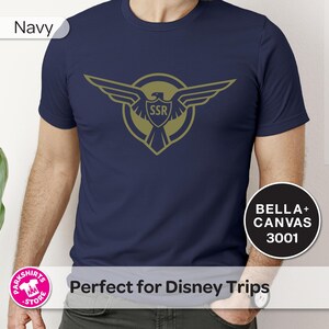 May include: Navy blue t-shirt with a gold emblem of an eagle and the letters "SSR". The shirt is a Bella+Canvas 3001 model. The t-shirt is a solid navy blue colour.