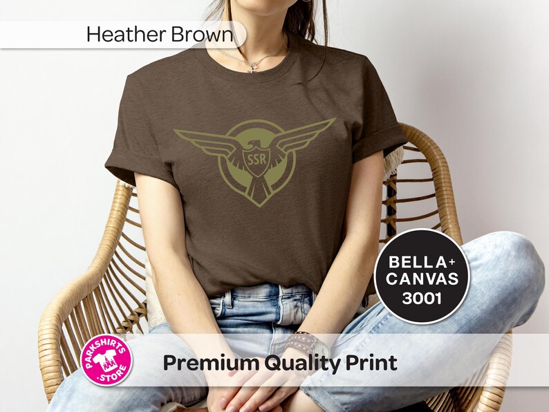 May include: Heather brown t-shirt with an olive green emblem of an eagle with outstretched wings and the letters "SSR". The shirt is made of Bella+Canvas 3001 material.