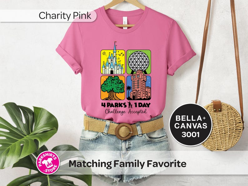 Puede incluir: Una camiseta rosa con un gr&aacute;fico que presenta cuatro iconos de parques tem&aacute;ticos: un castillo, una esfera geod&eacute;sica, un &aacute;rbol y una torre. El texto "4 Parks 1 Day Challenge Accepted" est&aacute; debajo. La camiseta est&aacute; en una percha.