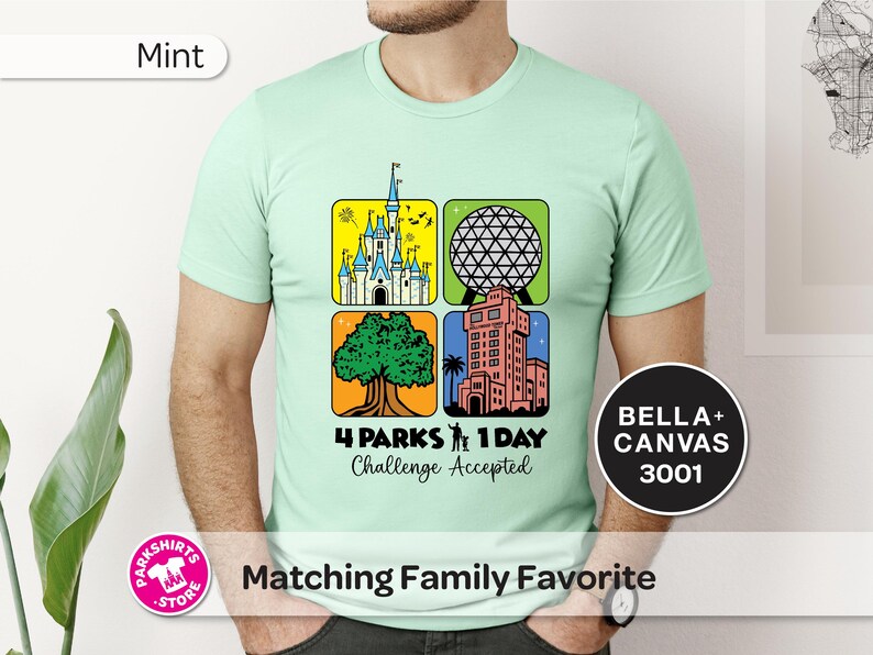 Puede incluir: Camiseta verde menta con un gr&aacute;fico colorido que presenta cuatro iconos de parques tem&aacute;ticos. El dise&ntilde;o incluye un castillo, una esfera geod&eacute;sica, un &aacute;rbol y una torre. El texto dice "4 Parks 1 Day Challenge Accepted".