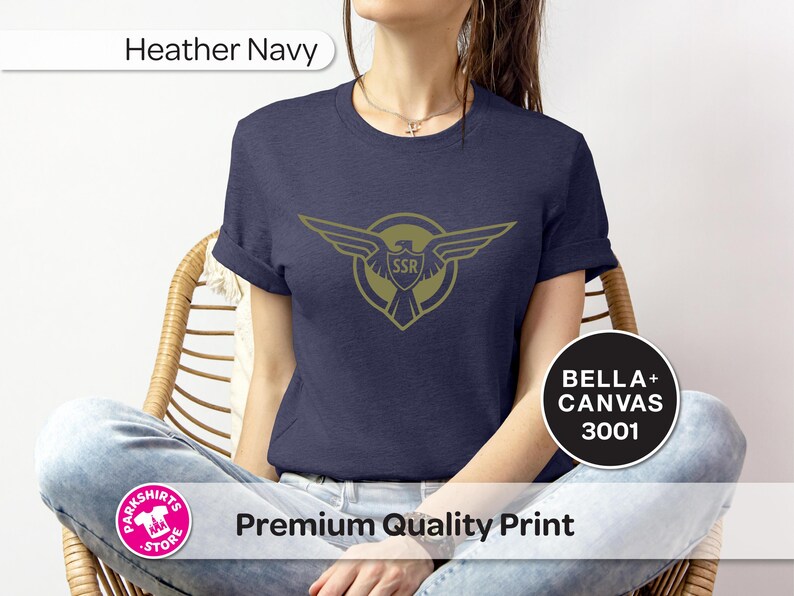 May include: Navy blue t-shirt with a gold emblem of wings and the letters "SSR". The shirt is made of Bella+Canvas 3001 material. The words "Premium Quality Print" are also visible.