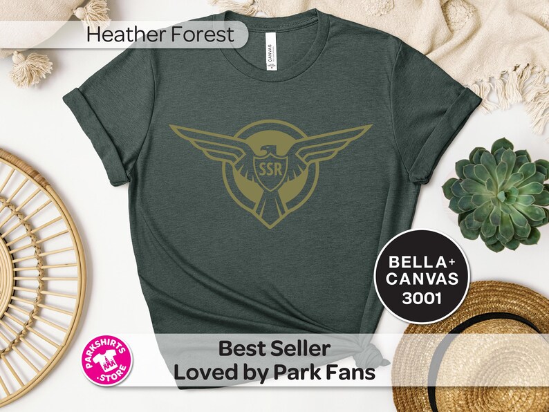 May include: A dark green t-shirt with a gold emblem featuring an eagle and the letters "SSR". The shirt has rolled-up sleeves and the text "Heather Forest" at the top. The text "Best Seller Loved by Park Fans" is at the bottom.