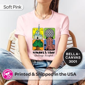 Puede incluir: Camiseta rosa claro con un gr&aacute;fico colorido que presenta cuatro iconos de parques tem&aacute;ticos. El dise&ntilde;o incluye un castillo, una esfera geod&eacute;sica, un &aacute;rbol y un edificio alto. El texto dice "4 Parks 1 Day Challenge Accepted."