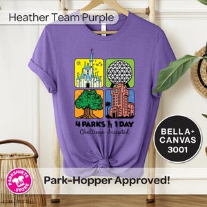 Puede incluir: Una camiseta morada con un gr&aacute;fico que presenta cuatro iconos de parques tem&aacute;ticos. El dise&ntilde;o incluye un castillo, una esfera geod&eacute;sica, un &aacute;rbol y una torre. El texto dice "4 Parks 1 Day Challenge Accepted". La camiseta es una Bella+Canvas 3001.