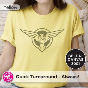 May include: Pale yellow t-shirt with a circular emblem featuring a stylized eagle and the letters "SSR". The shirt also has the text "Quick Turnaround - Always!" and the brand name "Bella + Canvas 3001".