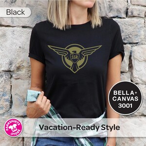 May include: Black t-shirt with a gold emblem featuring an eagle and the letters "SSR". The shirt is labelled "BELLA + CANVAS 3001" and "Vacation-Ready Style". The word "Black" is also displayed.
