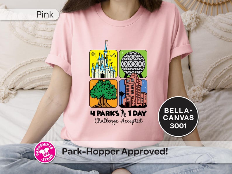 Puede incluir: Camiseta rosa claro con un gr&aacute;fico colorido que presenta cuatro iconos de parques tem&aacute;ticos. El dise&ntilde;o incluye un castillo, una esfera geod&eacute;sica, un &aacute;rbol y una torre, con el texto "4 Parks 1 Day Challenge Accepted". Hecha de Bella+Canvas 3001.