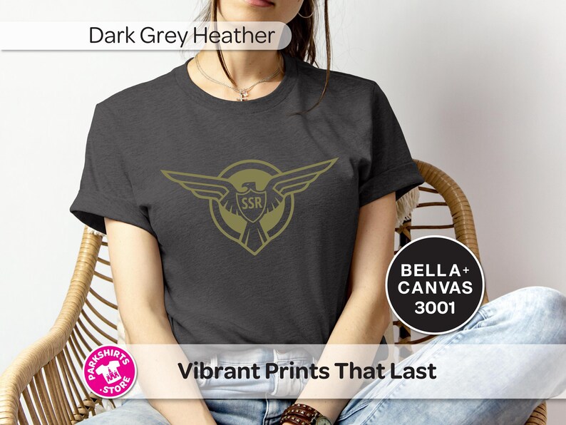 May include: Dark grey heather t-shirt with a gold emblem of wings and the letters "SSR" inside a shield. The shirt is labelled "BELLA + CANVAS 3001" and has the text "Vibrant Prints That Last".