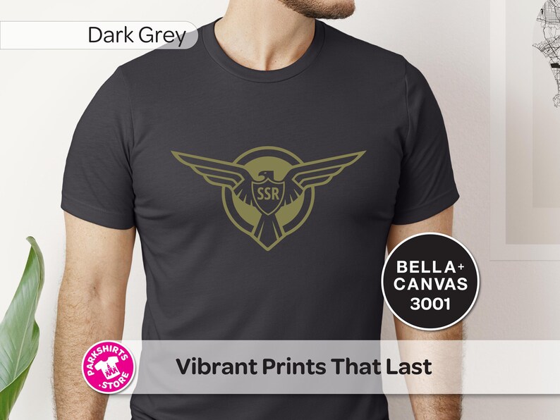 May include: Dark grey t-shirt with a gold eagle emblem and the letters "SSR". The shirt displays the text "Vibrant Prints That Last" and "BELLA + CANVAS 3001".
