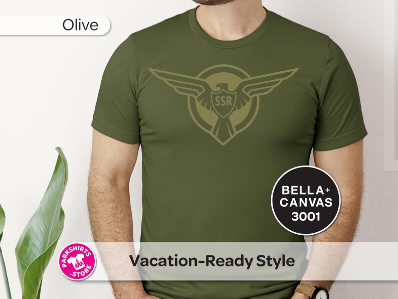 May include: Olive green t-shirt featuring an eagle emblem with "SSR" inside a shield. The shirt also has the text "Vacation-Ready Style" and the brand "BELLA + CANVAS 3001".
