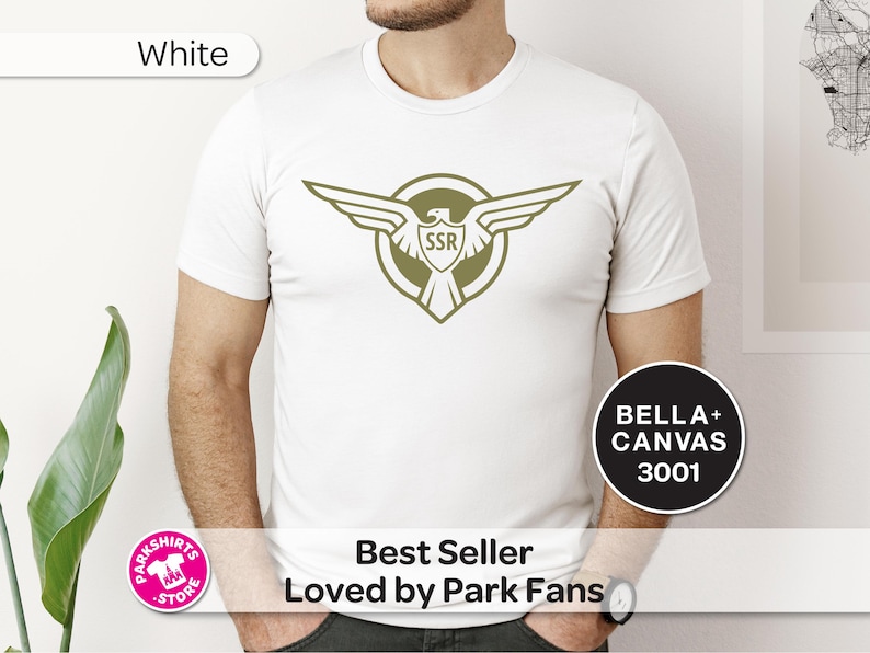 May include: White t-shirt with a green winged emblem and "SSR" within a shield. The shirt is a Bella+Canvas 3001. Text includes "Best Seller Loved by Park Fans". The shirt is a popular item.
