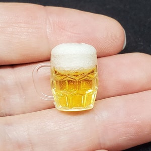 May include: A miniature glass mug filled with a yellow liquid and white foam, resembling a beer.
