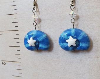 May include: A pair of blue and white seashell earrings with a white star on each shell. The earrings are made of polymer clay and have silver hooks.