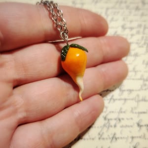 May include: A silver chain necklace with a small orange and white clay pendant shaped like a carrot with green leaves.