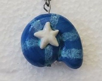 May include: A pendant necklace featuring a blue, snail-shaped charm with light blue horizontal stripes and a small, white, five-pointed star attached to the center. The charm hangs from a thin, silver-toned metal chain with small links.
