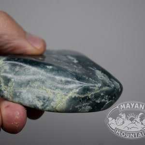May include: A smooth, green jade stone with white veins. The stone is shaped like a rounded rectangle and has a polished surface.