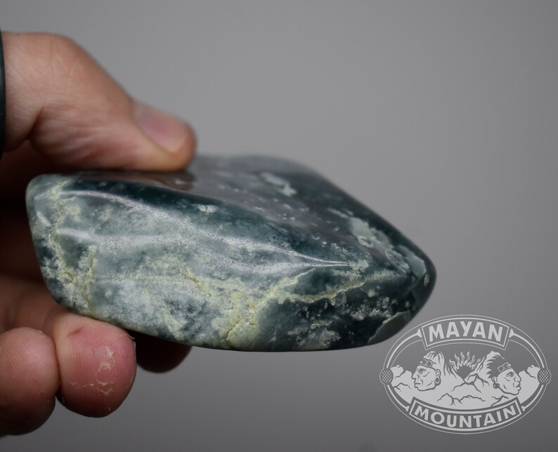 May include: A smooth, green jade stone with white veins. The stone is shaped like a rounded rectangle and has a polished surface.