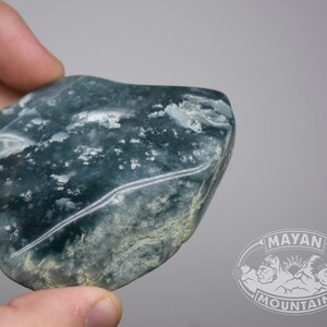 May include: A smooth, green and white jade stone with a mottled pattern. The stone is irregularly shaped and has a polished surface.