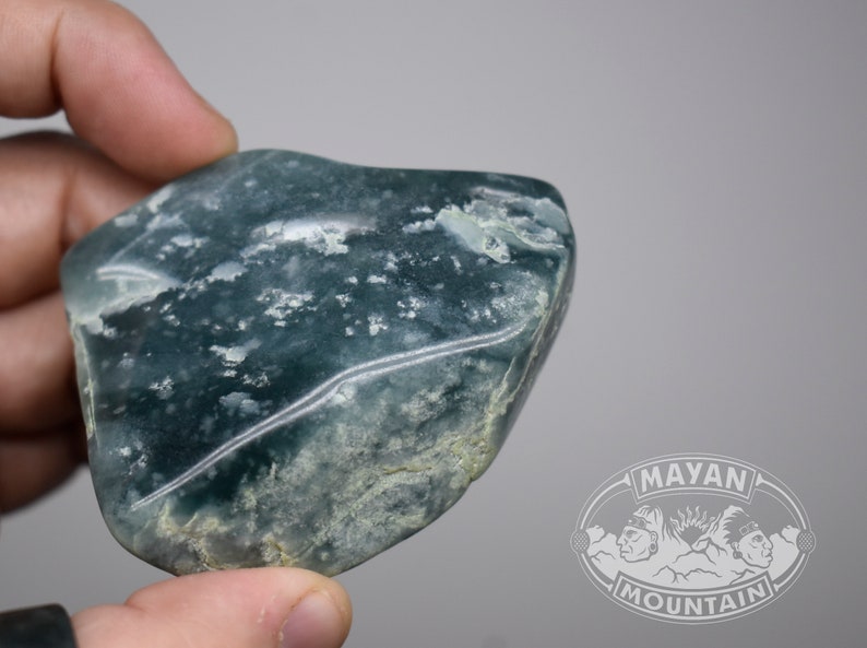 May include: A smooth, green and white jade stone with a mottled pattern. The stone is irregularly shaped and has a polished surface.