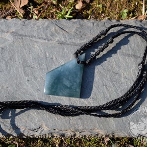 May include: A blue-green stone pendant necklace with a black braided cord. The pendant has a unique geometric shape. The necklace is displayed on a gray stone surface, with the "Mayan Mountain" logo visible in the bottom right corner.