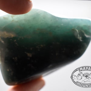 May include: A smooth, green, and black gemstone with a slightly irregular shape.