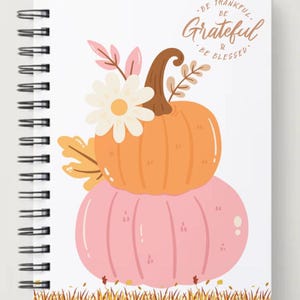 May include: Spiral-bound notebook with a fall-themed design. The cover features a stacked orange and pink pumpkin illustration, adorned with a white daisy and fall foliage. The text "Be Thankful, Be Grateful & Be Blessed" is written at the top.