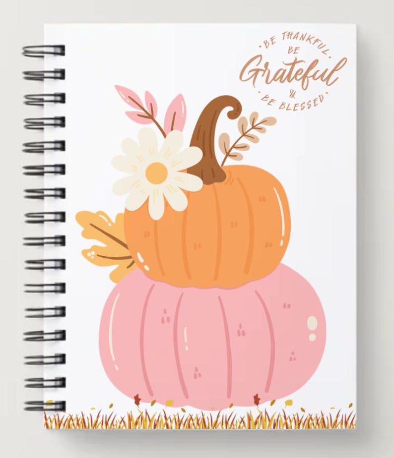 May include: Spiral-bound notebook with a fall-themed design. The cover features a stacked orange and pink pumpkin illustration, adorned with a white daisy and fall foliage. The text "Be Thankful, Be Grateful & Be Blessed" is written at the top.
