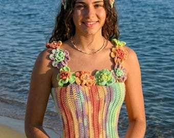 Pode incluir: Top e faixa de cabelo de crochê feitos à mão em cores pastel arco-íris. O top apresenta detalhes florais nas alças e decote. O fundo mostra uma massa de água.