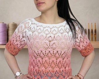 Pode incluir: Uma blusa de crochê de manga curta com um intrincado padrão rendado que transita da cor branca no decote para um rosa suave e coral profundo na bainha. A peça possui um decote redondo e uma bainha reta na altura dos quadris.