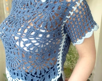 Pode incluir: Top de crochê azul com um padrão floral e mangas curtas. O top apresenta uma borda ondulada e é acentuado com acabamentos em azul claro e pequenas flores perto da gola. O design de tecido aberto é visível.