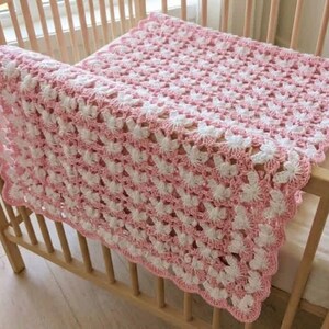 May include: A rectangular crochet blanket featuring a repeating pattern of white and light pink yarn. The textile has a scalloped edge border and an openwork design, showcasing a delicate, interconnected stitch structure throughout the piece.