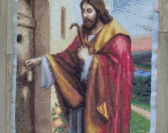 Pode incluir: Uma tapeçaria que retrata uma figura religiosa com cabelo castanho comprido, barba e auréola. A figura usa uma túnica vermelha e castanha e segura um cajado. O fundo mostra um edifício e uma paisagem com céu azul.