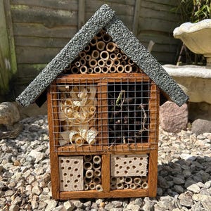 May include: A wooden insect house with a green roof. The house has multiple compartments with different materials for insects to nest in, including bamboo tubes, wood chips, and pine cones.