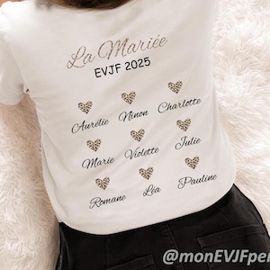 Op de afbeelding: Wit T-shirt met tekst en luipaardharten. De tekst luidt "La Mariée EVJF 2025" boven een reeks namen in een scriptlettertype, elk gecombineerd met een luipaardhart. De onderkant van het shirt heeft de Instagram-handle @monEVJFperso.