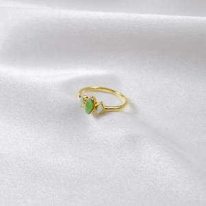 Puede incluir: Un anillo de oro con tres piedras verdes y blancas. Las piedras están engastadas en forma de marquesa.