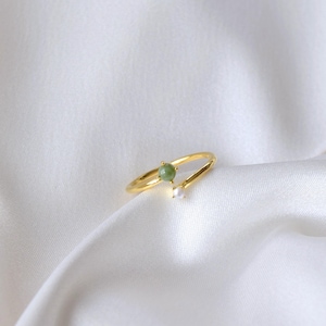 May include: A gold ring featuring a green gemstone and a white pearl. The ring has a curved band.