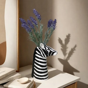 以下が含まれることがあります： 黒と白のシマウマの形をしたセラミックの花瓶に、紫色の花束が活けられています