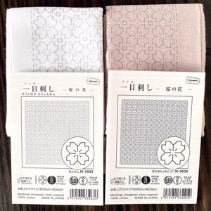 以下が含まれることがあります： 花柄の模様が施された、白とピンクの2枚の日本製ふきん。ふきんは綿100％で、サイズは約33cm×33cm。ふきんには「H-1033」と「H-3033」のラベルが付いています。