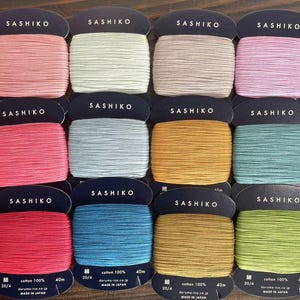 Peut inclure: Douze bobines de fil Sashiko de différentes couleurs, dont rose, gris clair, beige, bleu clair, jaune, sarcelle, rouge, bleu, or et vert. Chaque bobine est étiquetée "Sashiko" et contient des informations sur le fil, notamment la taille, le matériau et l'origine.