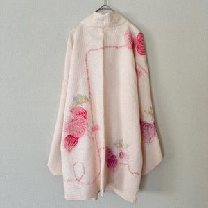 May include: A pale pink textured haori jacket featuring an open front and wide sleeves. The garment is decorated with embroidered floral motifs in shades of dark pink, magenta, and light green, arranged in a scattered pattern across the fabric.