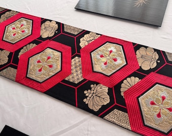 May include: A black and red table runner with gold floral and geometric patterns. The runner features red hexagonal shapes with gold and silver floral embroidery. The background is black with gold floral and geometric designs.