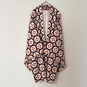 May include: A sleeveless jacket featuring a dark maroon and cream geometric pattern of repeating circles containing four-petaled shapes and small square grids. The garment has an open front design with a light-colored interior lining visible.