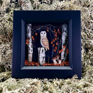 Peut inclure: Une œuvre d'art encadrée représentant un hibou perché sur une souche d'arbre dans une scène de forêt. Le hibou a un visage blanc et des plumes brunes et beiges. La forêt comprend des bouleaux, des feuilles orange et des champignons.