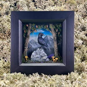 Puede incluir: Una obra de arte enmarcada que presenta un cuervo negro posado sobre una roca gris, con un fondo de bosque y montañas. La escena incluye árboles, setas y un cielo azul, todo dentro de un marco negro.